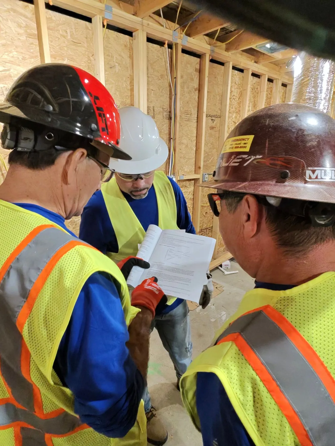 Tres alumnos con casco revisando juntos el manual dentro de la casa de práctica