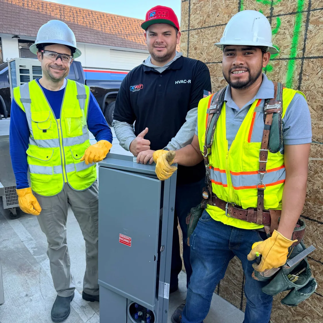 Tres alumnos con casco y chaleco junto a un tablero eléctrico con desconexión de emergencia